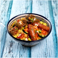 Een luchtige, gestoomde couscous, subtiel gekruid, met gegaard rundvlees, merguez en lamsgehakt. Aangevuld met een mix van verse groenten zoals courgette, pompoen, wortel, wittekool en zoete aardappel, plus kikkererwten, gekarameliseerde ui, rozijnen en shakshuka saus, en geurige bouillon. De groenten variëren met de seizoenen<br><br>